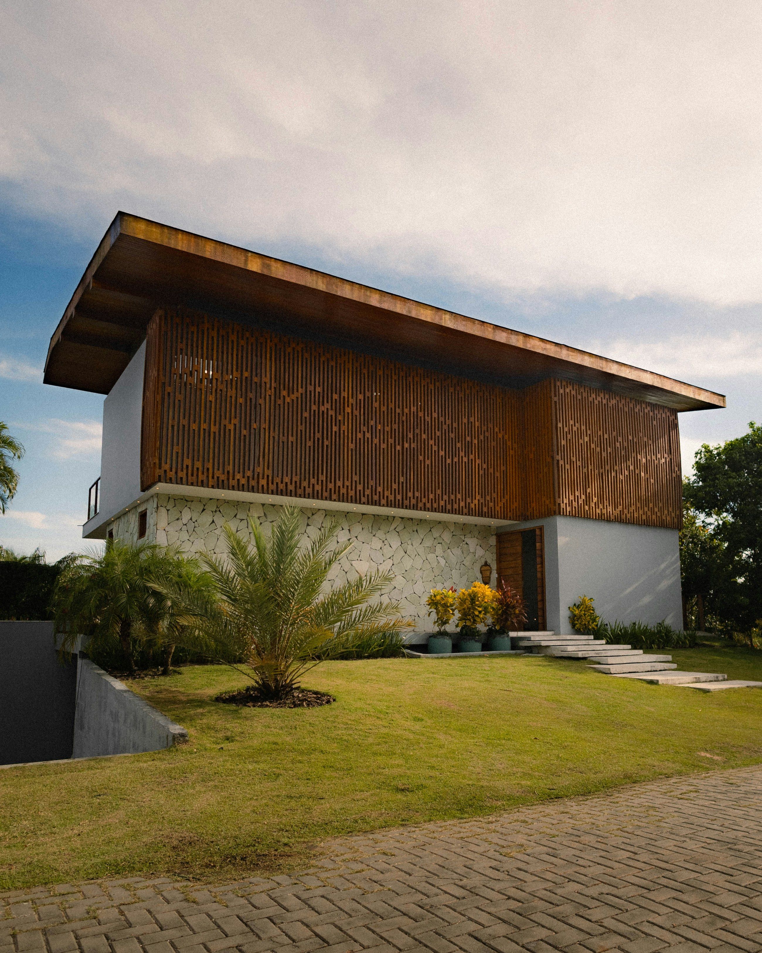 Casa de dois pavimentos com fachada em ripado de madeira, base em pedra natural e jardim tropical (imagem meramente ilustrativa, não é obra do escritório)